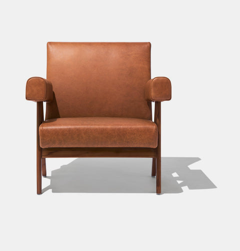 Caramel brown leather lounge chair with leather armrests and solid ash wood legs stained walnut.