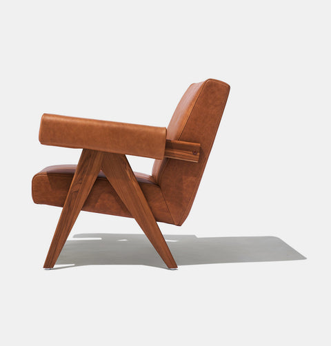 Caramel brown leather lounge chair with leather armrests and solid ash wood legs stained walnut.
