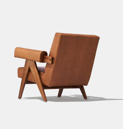 Caramel brown leather lounge chair with leather armrests and solid ash wood legs stained walnut.