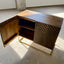 Dark brown mango wood sideboard with a CNC carved repeating pyramid pattern on the two doors. Brass finished iron legs & frame. One door open.