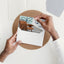 Man's hands at a desk putting a Qubik Furniture gift card worth a 250$ value into a white envelope.